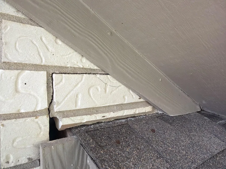 Brick separation near a window frame and roofline